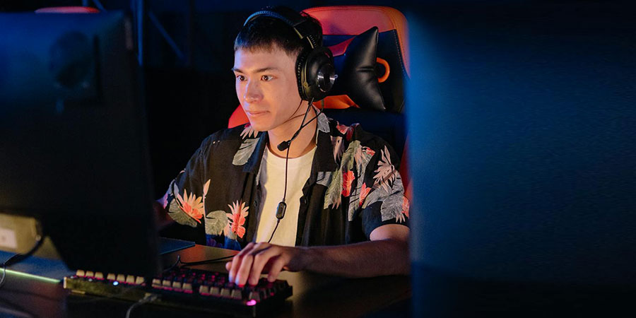 man wearing floral shirt sitting on a gaming chair, in front of a computer while using the keyboard